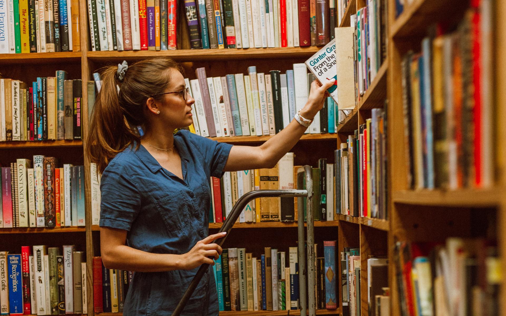 Junge Frau auf einer Leiter vor dem Bücherregal