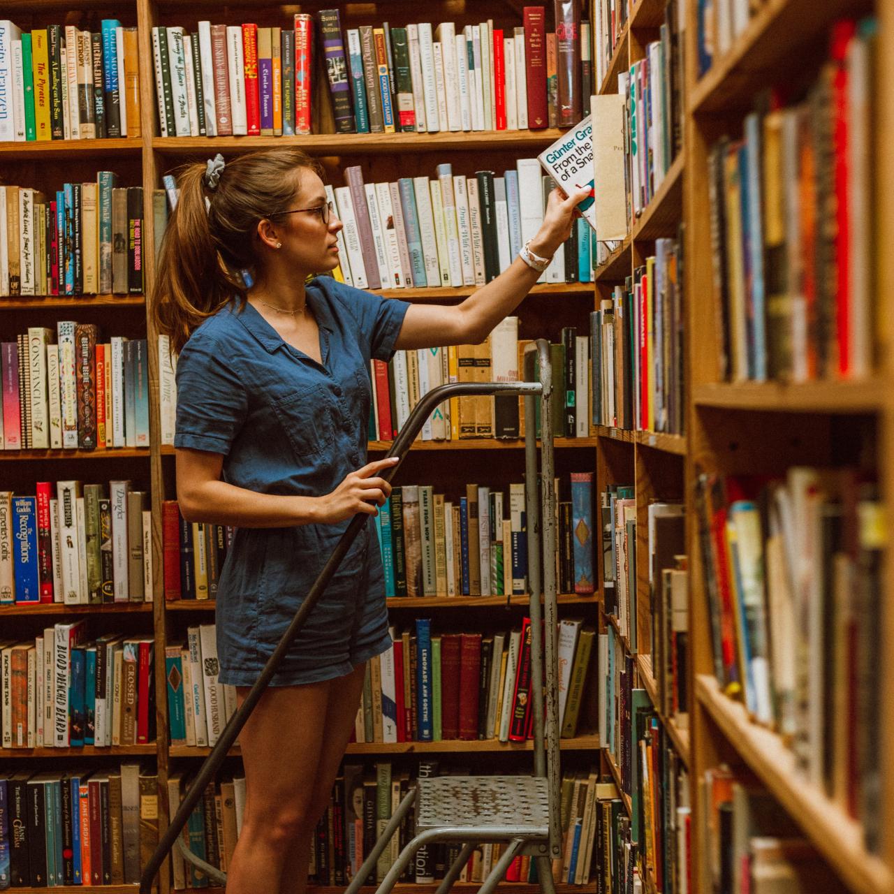Junge Frau auf einer Leiter vor dem Bücherregal